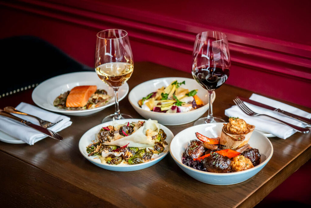 The Dorset Winterlicious dishes and glasses of wine on a dark wood table in front of the a maroon wall