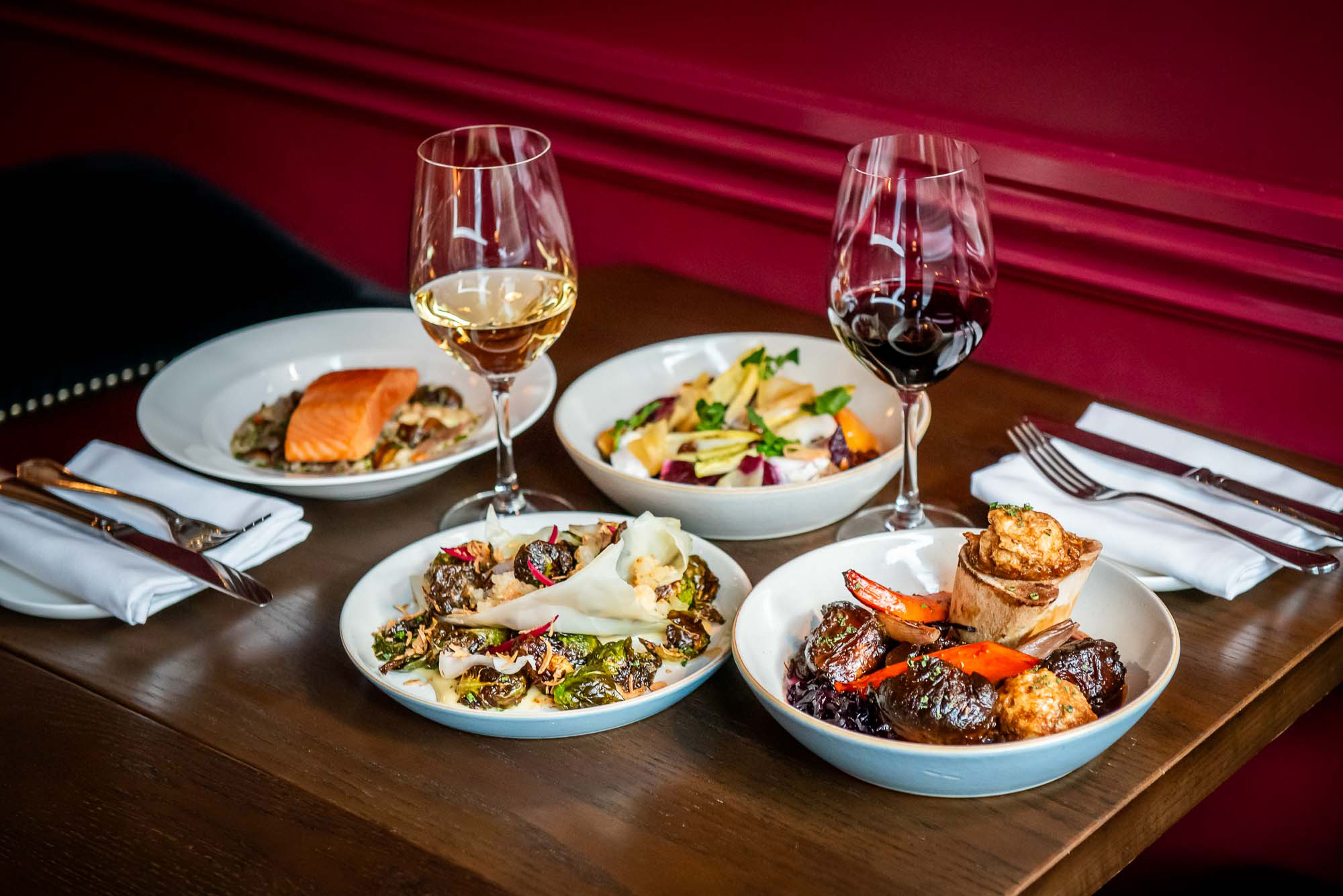 The Dorset Winterlicious dishes and glasses of wine on a dark wood table in front of the a maroon wall